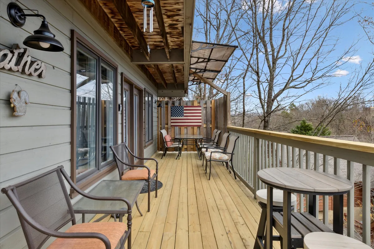 A spacious wooden deck adorned with an American flag, comfortable seating, and charming wind chimes. The deck provides ample space for groups to socialize or relax while taking in the fresh air and beautiful views, embodying both comfort and a sense of place.