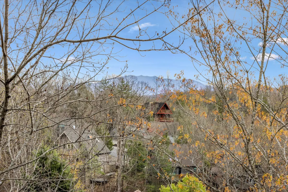A tranquil scene featuring distant mountains, vibrant autumn foliage, and a glimpse of cabin architecture at sunset. The image conveys the vastness of nature, the changing seasons, and the welcoming presence of the cabin nestled in the Smokies.
