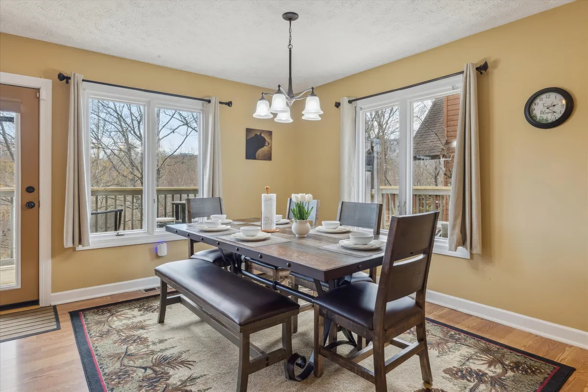 A spacious dining area adorned with a large, beautifully set dining table beneath a chandelier, surrounded by ample seating and illuminated by natural light from generous windows. Decorative artwork adds warmth and personality to the space, inviting guests to come together for shared meals and stories.