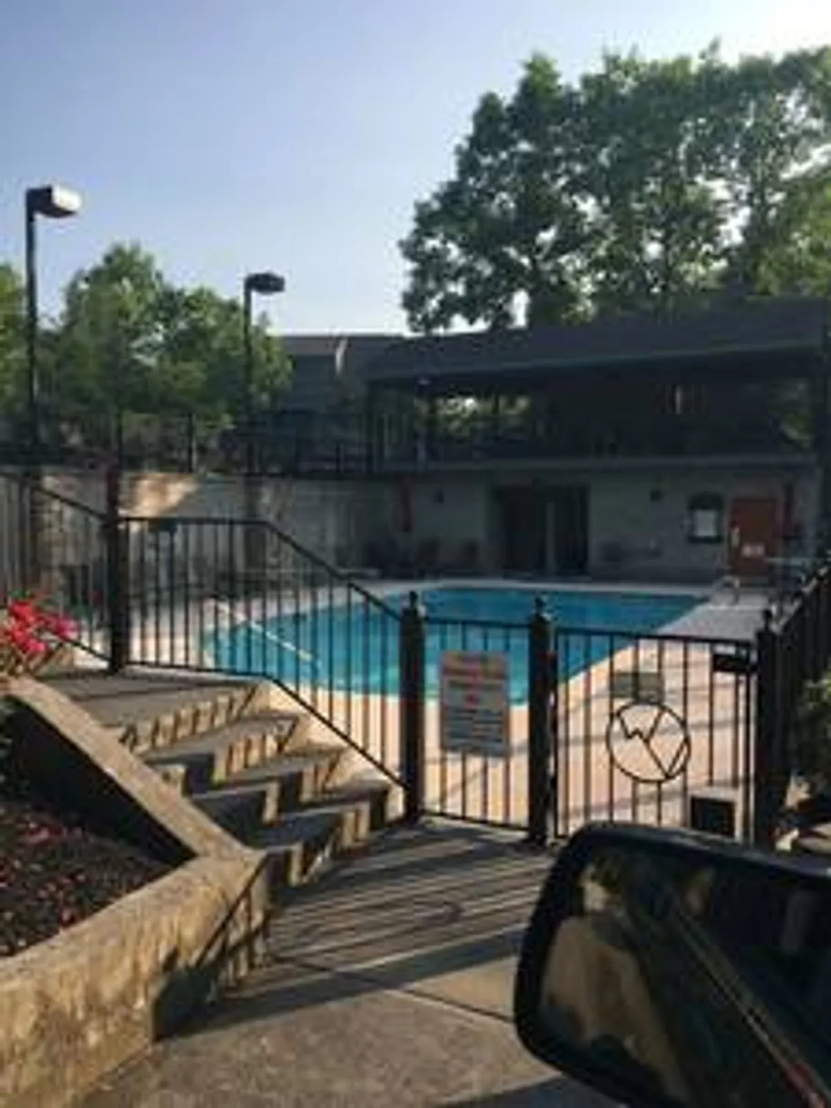 This image features a sparkling swimming pool surrounded by a well-maintained fence, steps leading down to the pool area, and lush landscaping with colorful flowers. The setting is inviting for swimming, sunbathing, and poolside gatherings, evoking a sense of summer fun and refreshment.