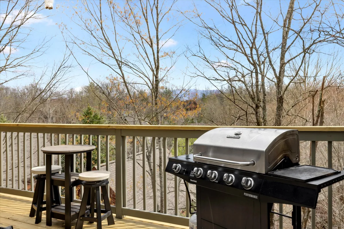An outdoor deck scene with a barbecue grill, inviting seating, and a panoramic scenic backdrop, ideal for outdoor dining or relaxing with friends and family. The view suggests mountain vistas and fresh air.