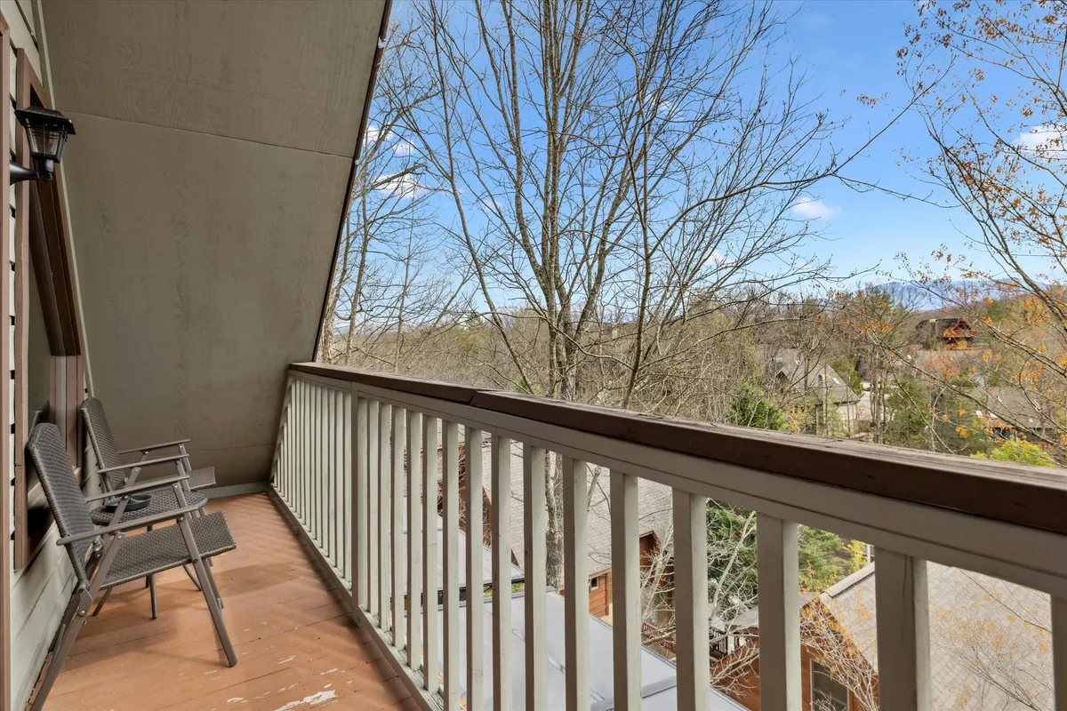 A private balcony featuring two metal chairs and a railing, overlooking a peaceful view of treetops and neighboring cabins. The setting suggests a quiet spot perfect for morning coffee or watching the sunset, with a backdrop of natural beauty.
