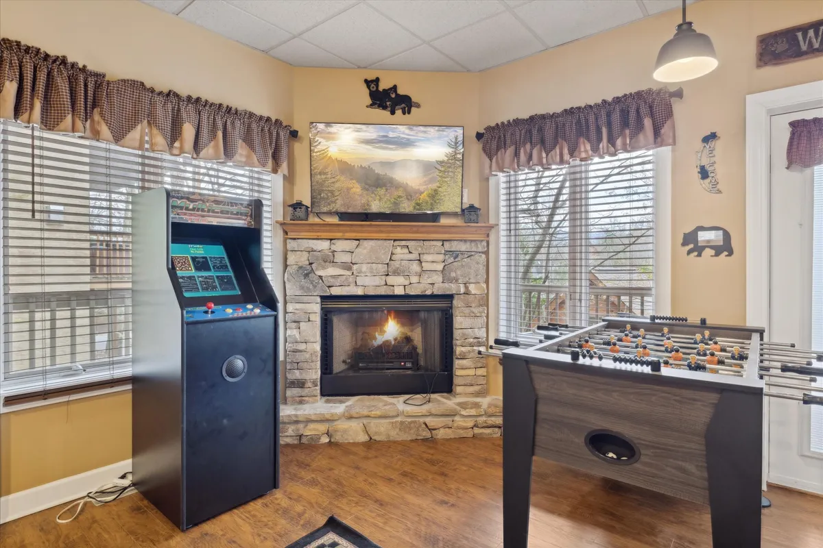This lively interior captures a dedicated game area featuring an arcade game machine, a foosball table, a cozy fireplace, and a television. The playful setup is enhanced by the warmth of the fire, inviting seating, and entertainment options, showcasing the room as a true hub for fun and relaxation.