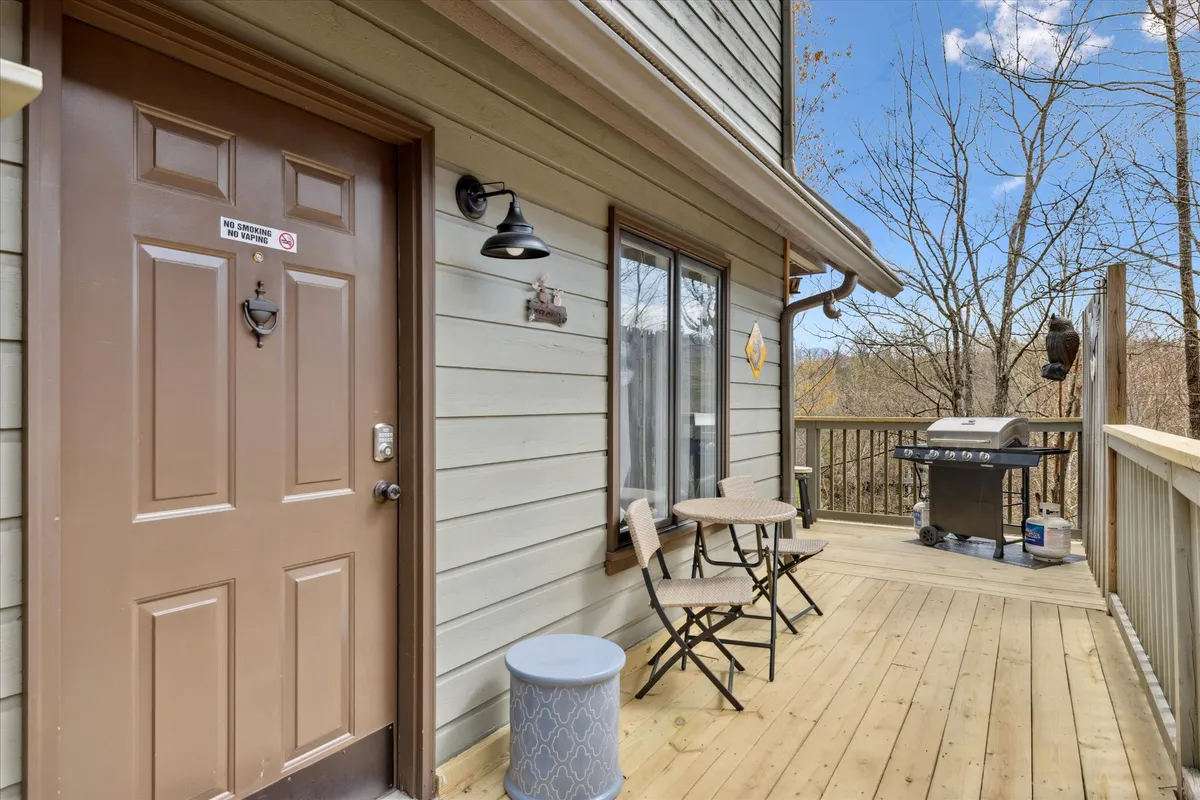 An inviting cabin exterior showcasing the front door, cozy outdoor seating, and a grill. The deck overlooks nature, suggesting a peaceful spot to unwind after adventurous days.