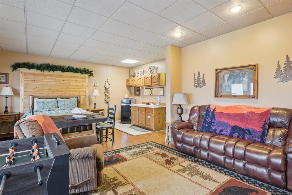 A comfortable, homey space where a wooden bed, foosball table, leather sofa, and kitchenette come together. The foosball table sits prominently, with the surrounding furniture inviting groups to play, snack, and socialize in a relaxed setting.