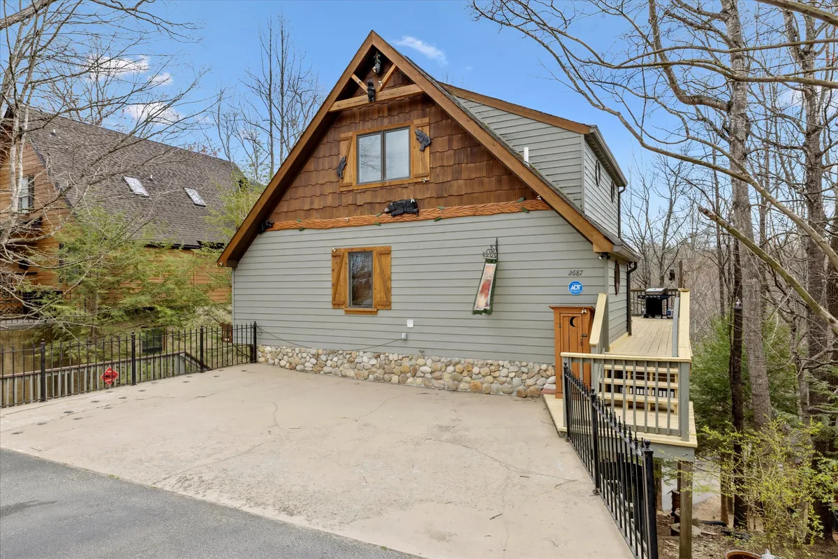 This image features the A-frame architecture of the cabin, its stone foundation, and a cozy deck area surrounded by trees. The inviting exterior highlights outdoor gathering space ideal for groups and families. The atmosphere is tranquil, with soft evening light suggesting both relaxation and togetherness.