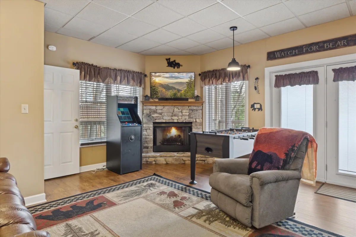 A dynamic interior scene centered around an arcade machine, foosball table, fireplace, and recliner. The arrangement suggests a casual, social environment perfect for tournaments, storytelling, and relaxation after a day of adventure.